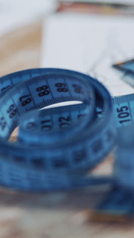 workplace of a seamstress on the table with some sketches and meter. creative drawings of a tailor on white papers and a blue tape measure on the wooden background. close-up. vertical video