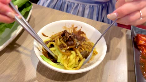 close-up of hands mixing jajangmyeon noodles with chopsticks in a vibrant bangkok setting. bright lighting enhances the colorful dish
