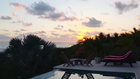 drone flies over luxurious pool in private beachside ocean front villa, and up towards the beach at sunset