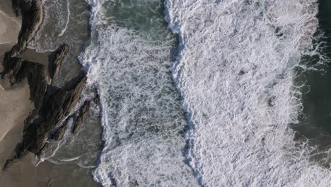 large waves roll onto a secluded beach breaking over a texture rock formation