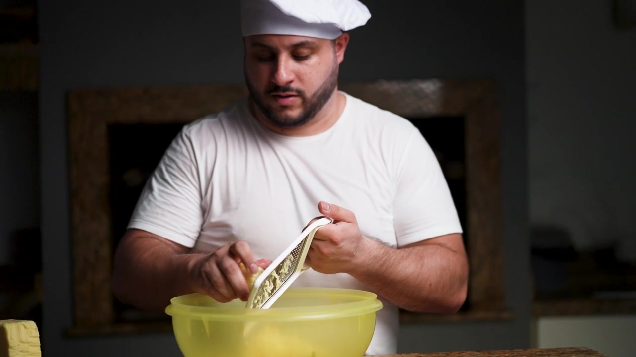 Un'inquadratura a mezzo busto di uno chef che grattugia il formaggio in una cucina calda e casalinga