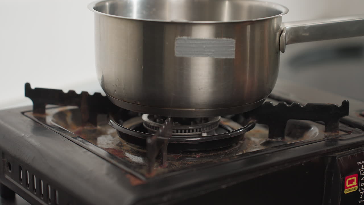 Close up of female hand with polished nails carefully placing stainless steel pot on gas burner and turning on flame, preparing to start cooking in clean modern kitchen