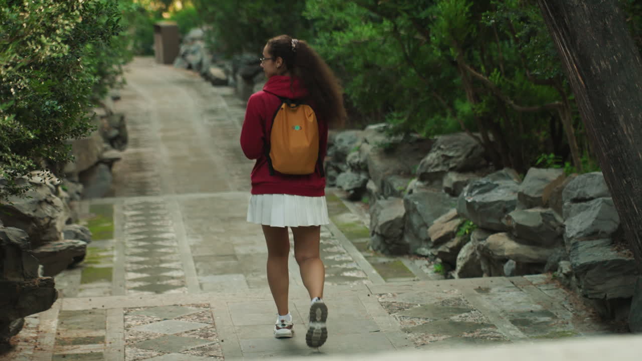 Wanita menjelajahi jalur hutan sendirian. Wanita sendirian dengan ransel berjalan di samping aliran sungai dan pepohonan. Pendaki wanita mandiri bergerak melalui tanaman hijau lebat dan di sepanjang aliran air yang tenang di hutan.