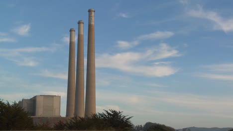 a time lapse shot of clouds moving behind the smokestacks of a power plant