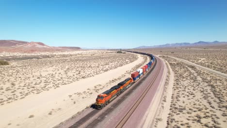 un tren de carga rodando por la vía en un paisaje desértico - vista aérea del motor tirando de los coches que desaparecen en la distancia