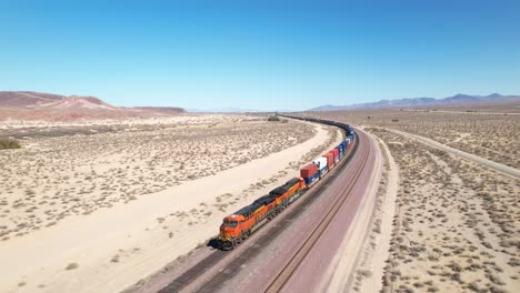 a freight train rolling down the track in a desert landscape - aerial view of the engine pulling cars that disappear into the distance