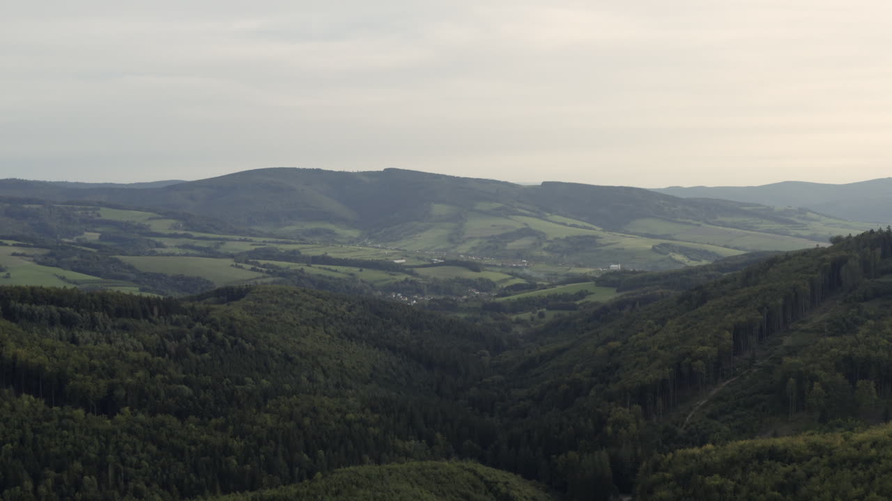 Ripresa aerea lenta in avanti di verdi colline boscose nell'Europa centrale rurale.