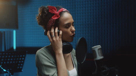 primer plano de la joven cantante bonita y sonriente cantando en el micrófono en el estudio y luego sonriendo a la cámara