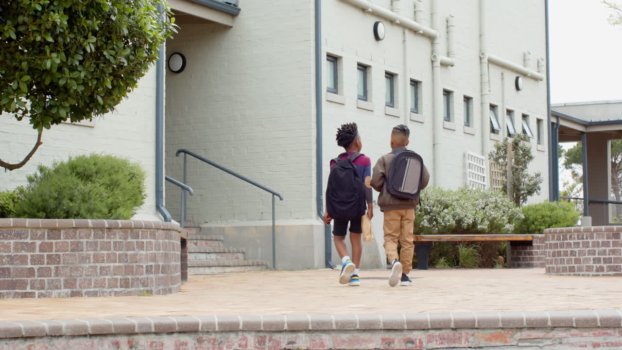Multiracial boys with backpacks walking towards school building, ready for new day