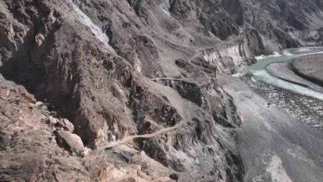 Aerial-View-Of-Winding-Old-Silk-Road-Through-Rugged-Arid-Mountains-Beside-River