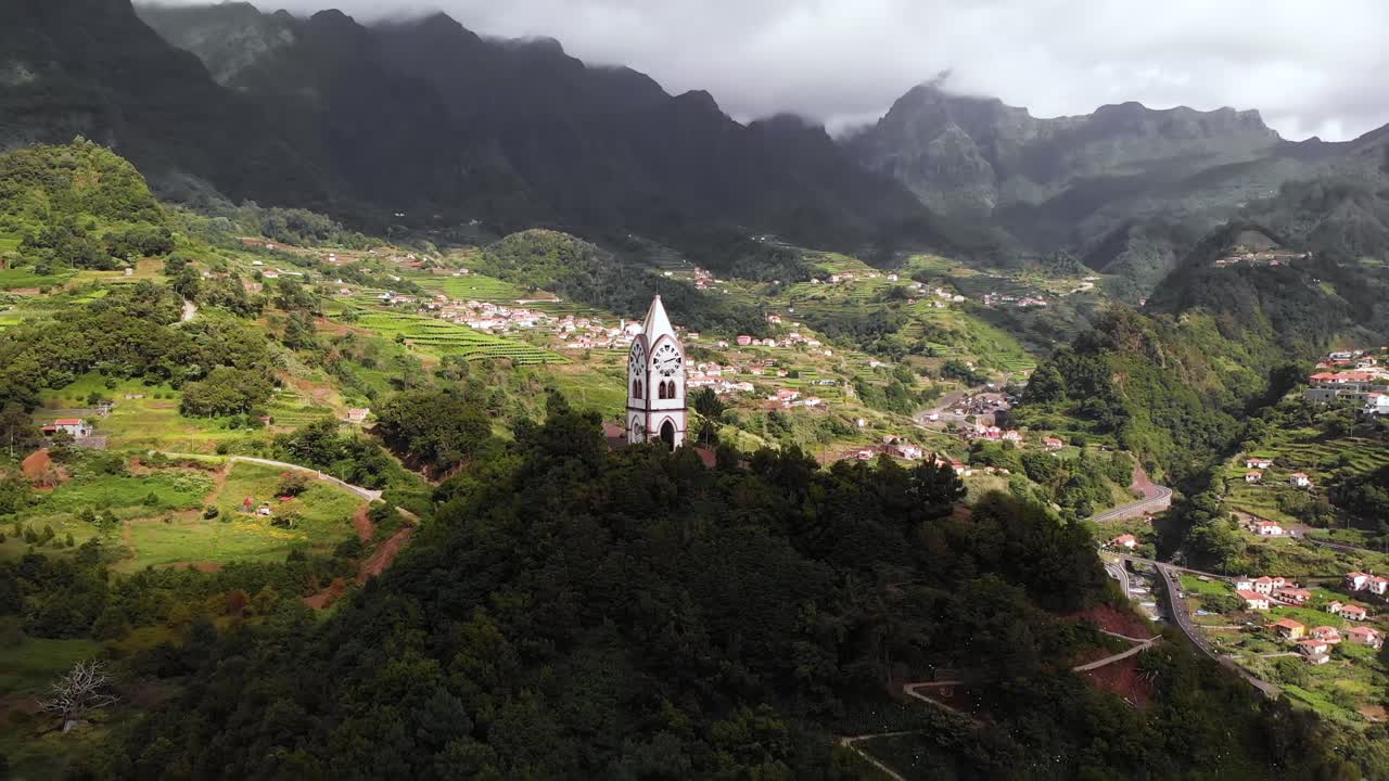 Ripresa aerea che rivela un'antica cappella sulla cima di una collina verde con paesaggio montano sullo sfondo, Sao Vicente, Madeira