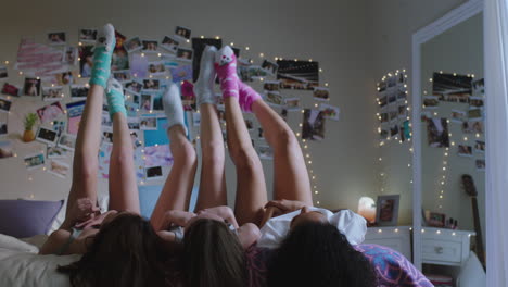 happy teen girls lying on bed at home with legs up having fun wiggling feet hanging out wearing pajamas enjoying relaxing morning on weekend