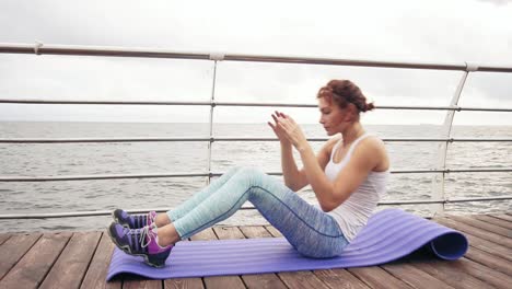 Young athletic woman doing situps on the mat by the ocean in the early morning. Fitness woman doing abs crunches. Abs workout
