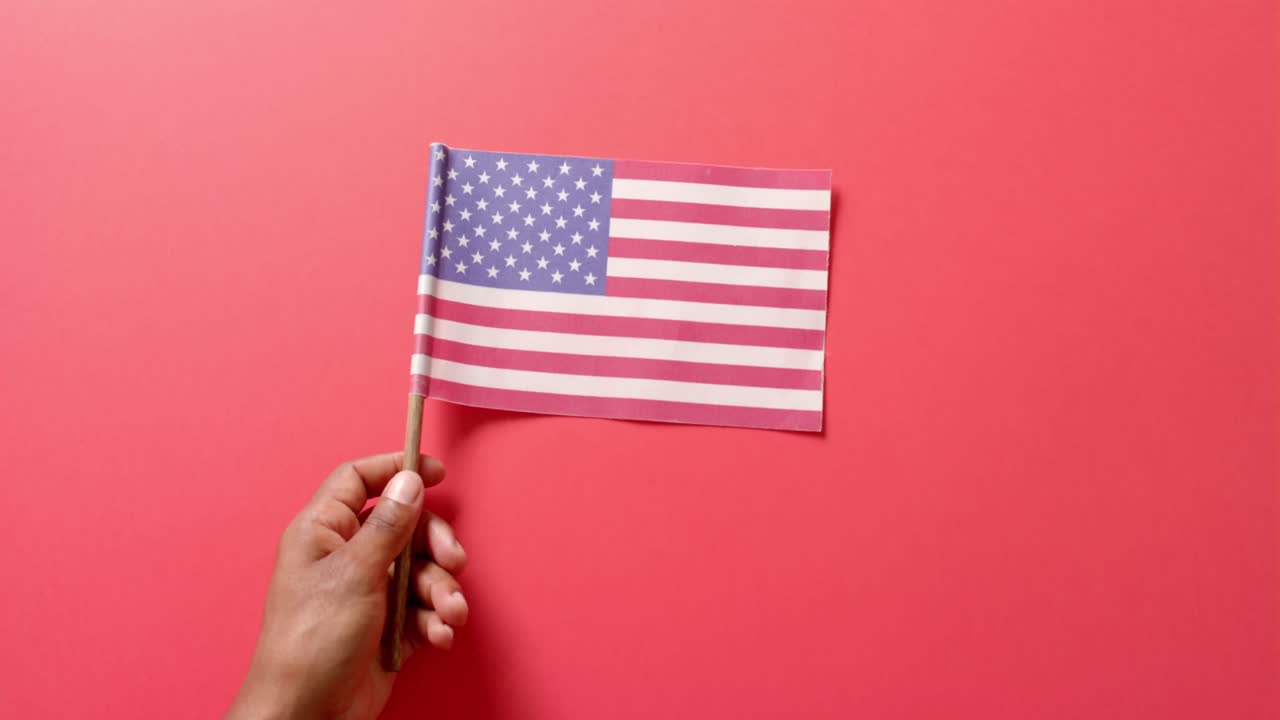 cerca de la mano sosteniendo la bandera nacional de los ee.uu. en fondo rojo.