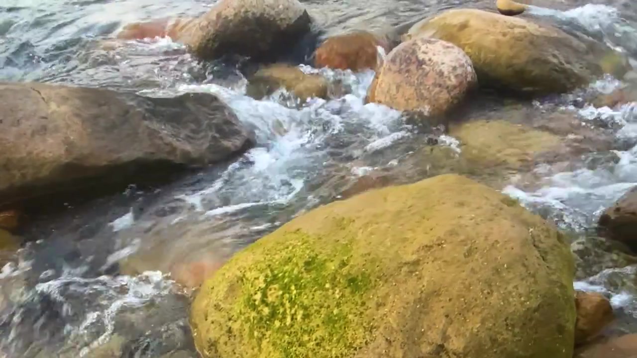 Scenic natural rocky river stream flows through boulders - panning shot.