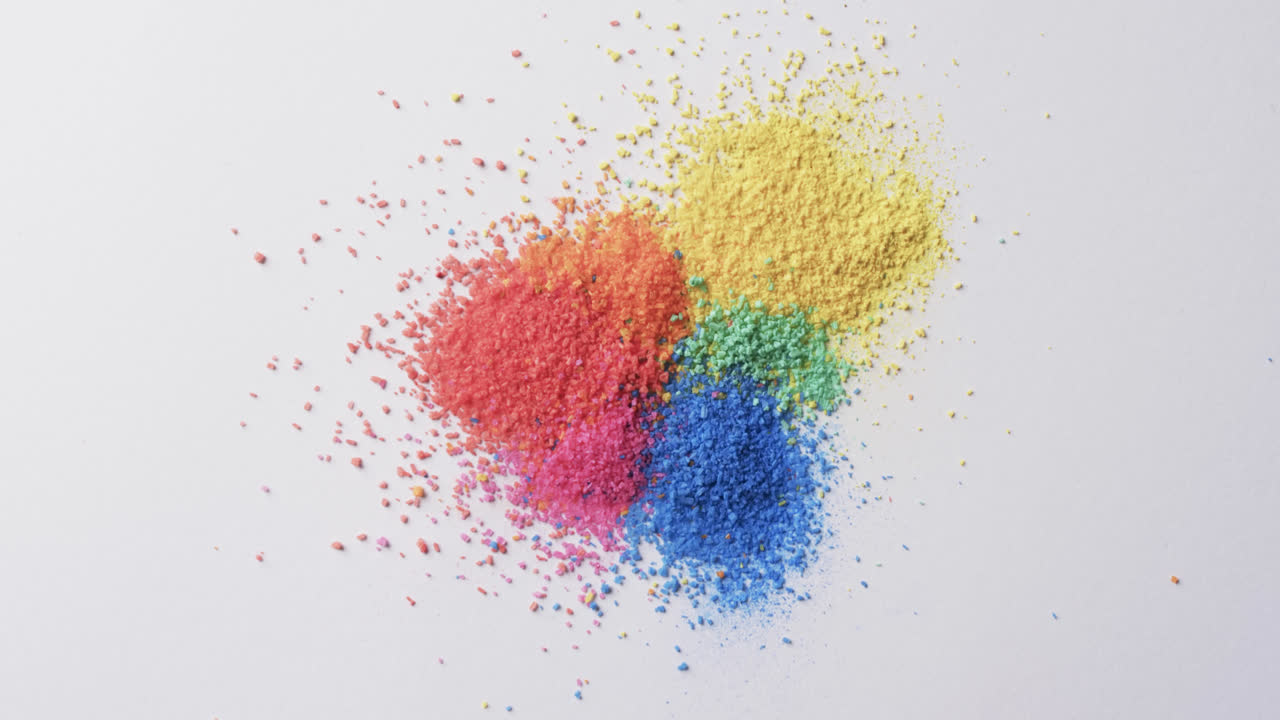 Video of close up of multi coloured sand grains and copy space on white background