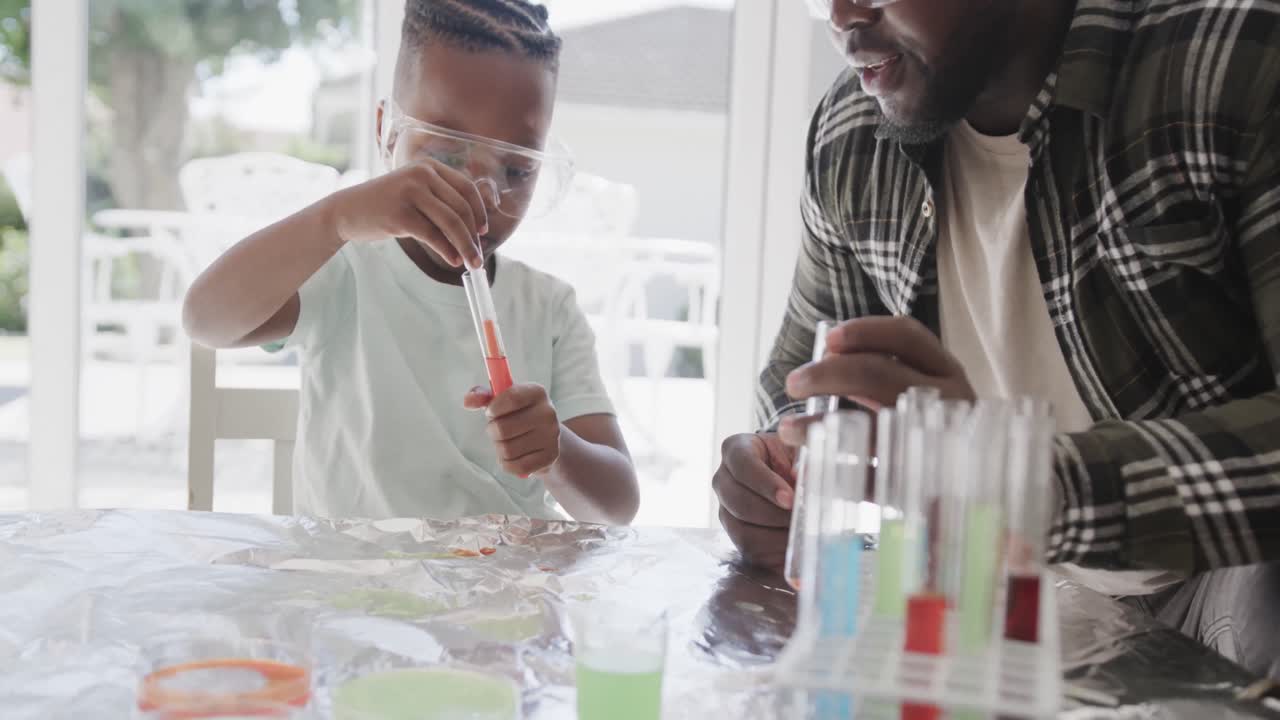 padre y hijo afroamericanos sentados en la mesa sosteniendo tubos de ensayo con líquido, en cámara lenta