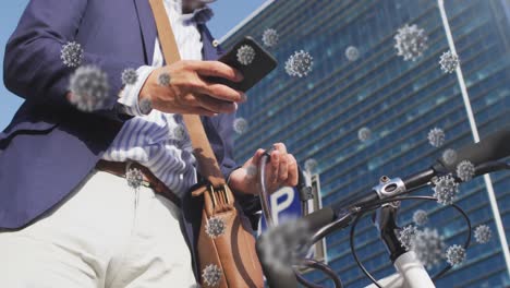 animation of covid-19 cells over asian man wearing face mask with bicycle using smartphone outdoors