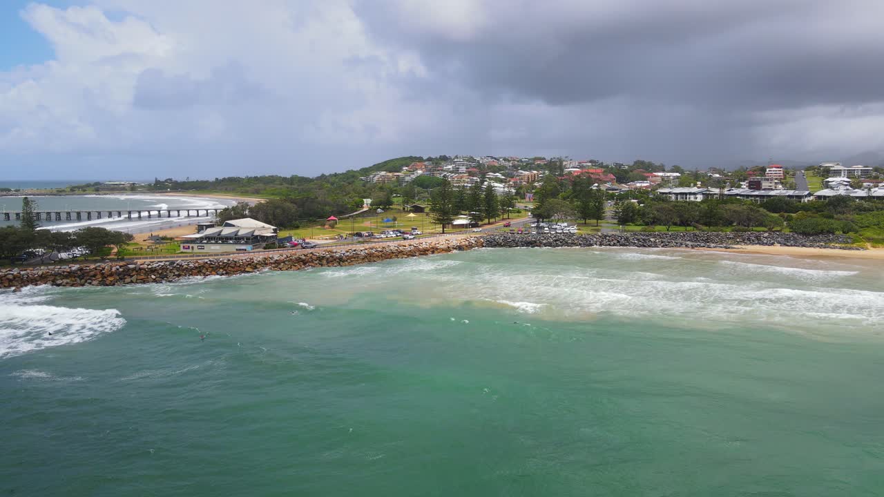 la gente nada en el océano con automóviles que viajan en marine drive - embarcadero del puerto de coffs y parque marino de islas solitarias con cielo nublado en nsw, australia