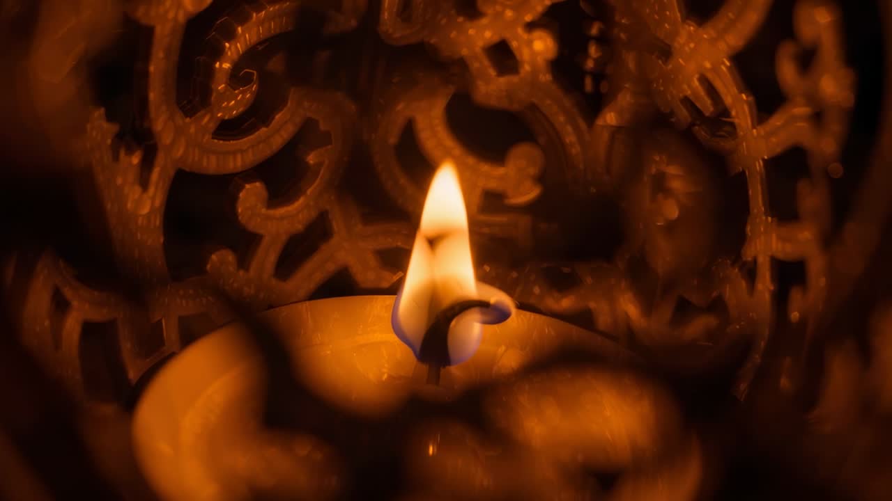 Flickering candle flame dancing in gentle breeze inside ornate lantern, casting scrollwork shadows