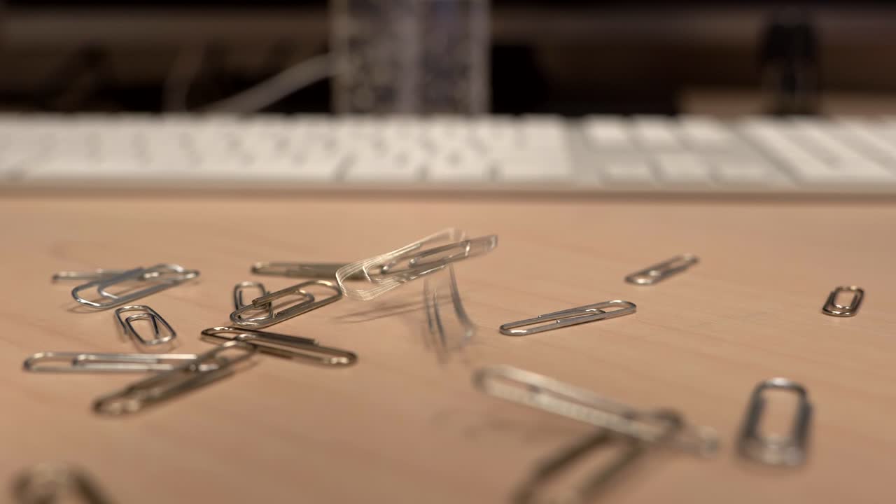 una mano llena de clips de papel que caen lentamente sobre un escritorio de oficina en cámara lenta, poco a poco