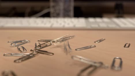 a hand full of paper clips slowly dropping onto an office desk in slow motion a little bit at a time