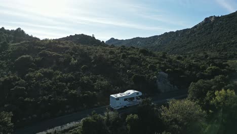 white rv camping car, camper van drives uphill green mountains, valley landscape in pyrenees summer, aerial drone establishing shot