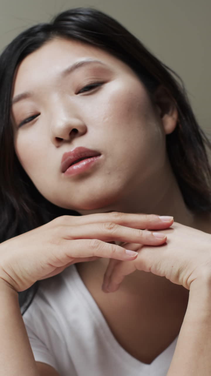 Vertical video of asian woman with black hair and make up touching face, copy space, slow motion