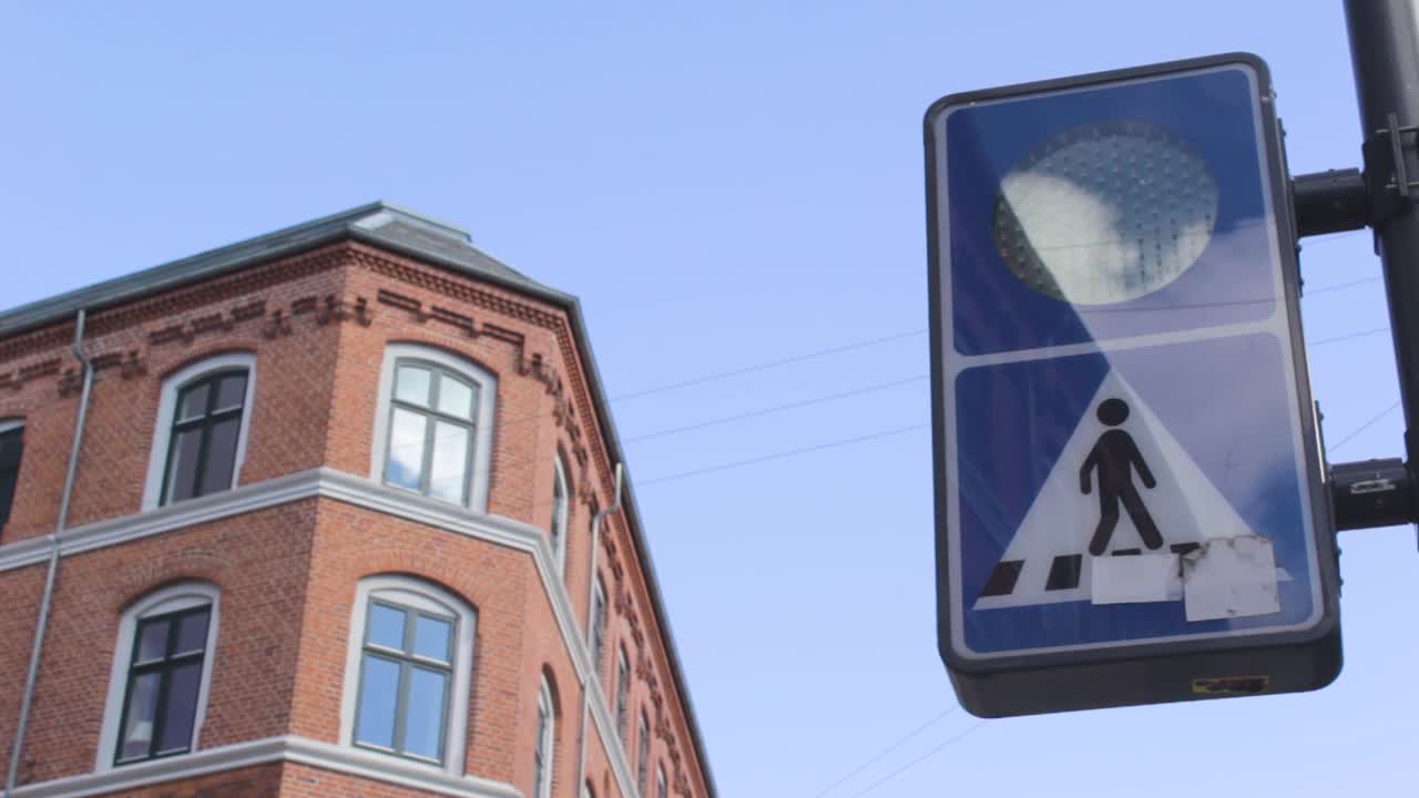 Orange Crosswalk warning light flashing on the street. View from below with bricks building on the left and traffic light on the right. Copenaghen, Denmark