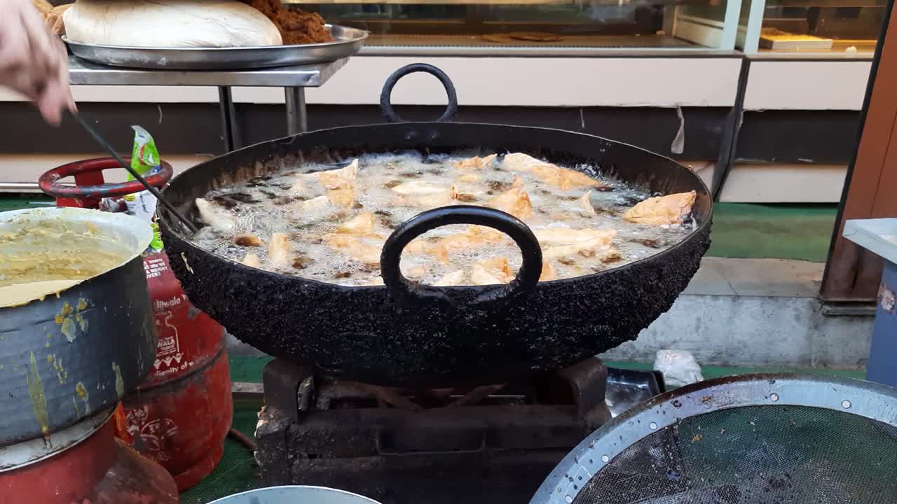 An Indian street vendor prepares snacks Samosas frying in oil at Ramadhan market in India. Making Of Delicious And Crunchy Samosas. Closeup Of Bubbles In Oil In Making Of Samosas. deep frying samosa