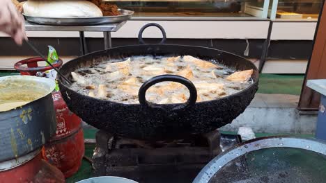 an indian street vendor prepares snacks samosas frying in oil at ramadhan market in india. making of delicious and crunchy samosas. closeup of bubbles in oil in making of samosas. deep frying samosa