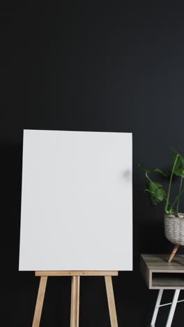 vertical video of white canvas sign on wooden easel with copy space on black background