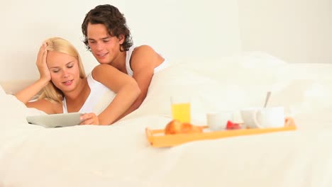 pareja feliz juntos en la cama con desayuno y tableta