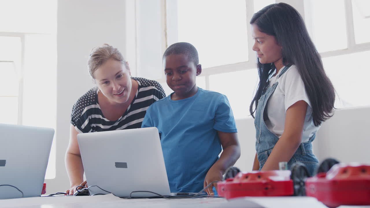 estudiantes con una maestra en una clase de codificación de computadoras después de la escuela aprendiendo a programar un vehículo robot