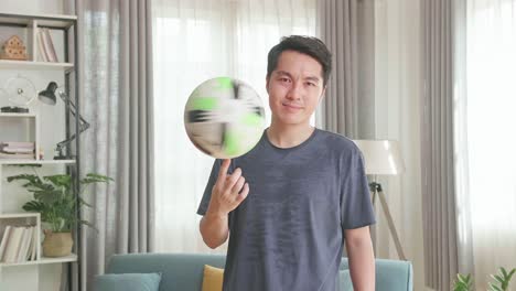 asian man spin soccer ball on finger in living room