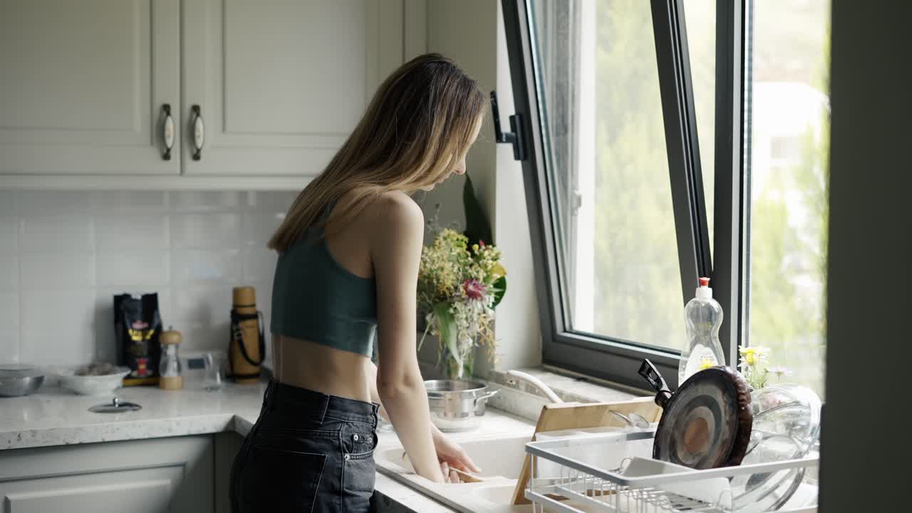 Donna che lava i piatti sotto l'acqua corrente nel lavello di una cucina moderna.