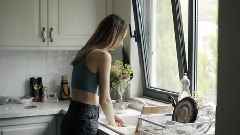 Woman-washing-dishes-under-running-water-in-sink-at-modern-kitchen