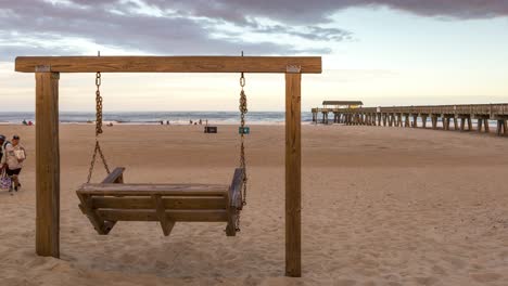 Holzschaukel-Und-Menschen,-Die-Bei-Sonnenaufgang-Am-Strand-In-Der-Nähe-Des-Tybee-Pier-Spazieren-Gehen