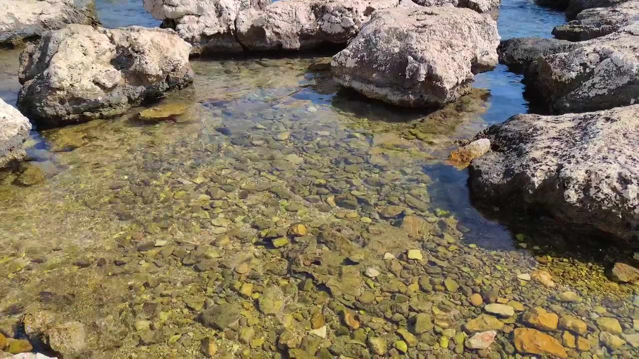 Acqua limpida e poco profonda e costa rocciosa in una giornata di sole