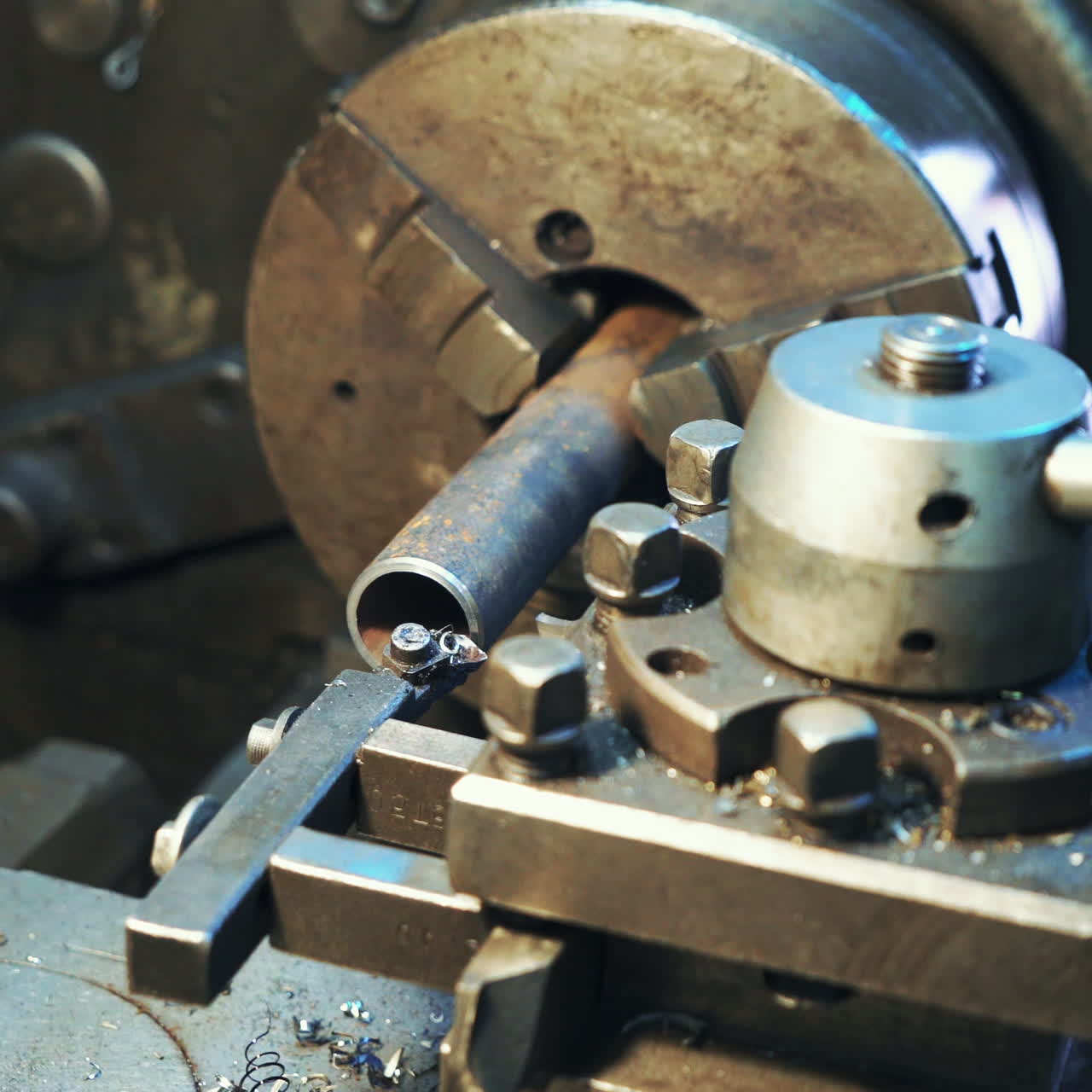 A lathe processes metal blank in the factory. Shavings fall to the floor in the room.Close-up.