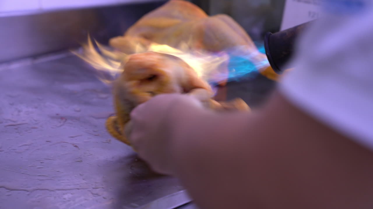 A chef  burning  the plumage of a chiken on  a table  in a kitchen , before prepre with him a good meal