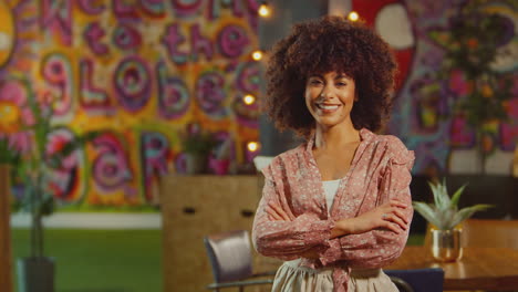 Portrait-Of-Smiling-Female-Server-Or-Owner-Wearing-Apron-Walks-Into-Focus-In-Cool-Bar-Or-Club