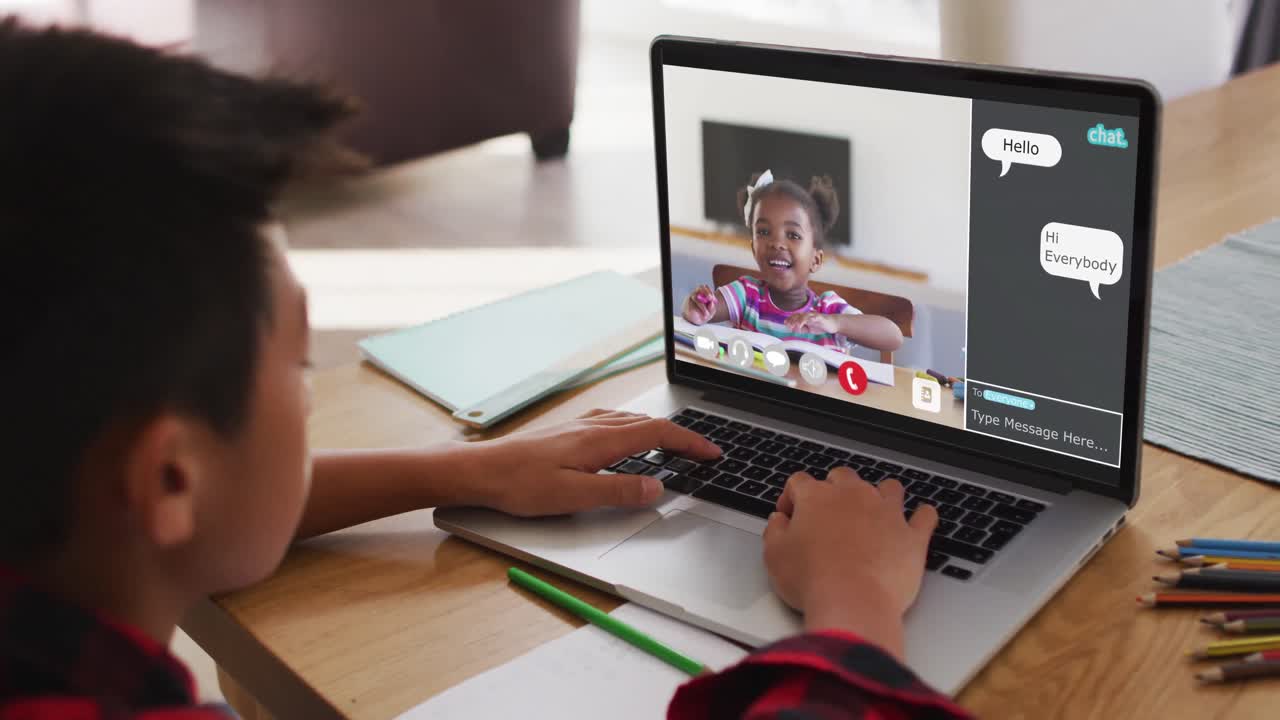 Schoolboy using laptop for online lesson at home, with girl raising hand and webchat on screen