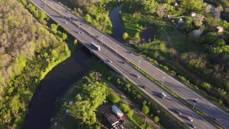 drone tracking shot of congested highway surrounded by green forest trees and river in suburb area of buenos aires - beautiful weather with sunlight in the evening