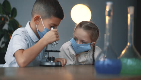 little boy and girl with face mask using a microscope. kids and science.