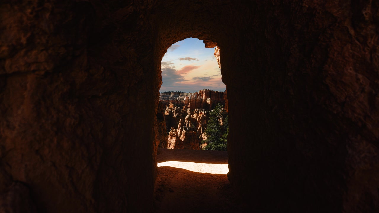 View through dark rock tunnel framing hoodoos and blue sky in Bryce Canyon time lapse. Utah, USA.