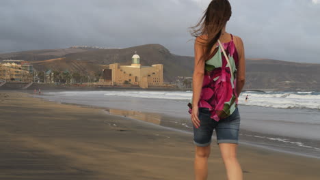 Plano-Cinemático-Al-Amanecer-De-Una-Mujer-Paseando-Por-La-Playa-De-Las-Canteras-Y-Al-Fondo-Se-Ve-El-Auditorio-Alfredo-Kraus