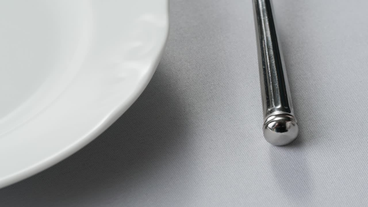 Professional table setting with white gloves. Plates, fork, knife, and glass arranged on a white table.