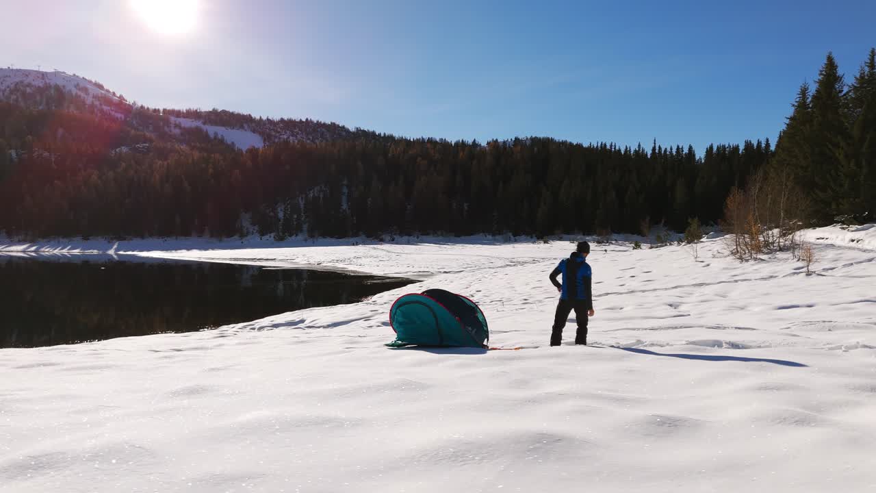 hombre lanzando una tienda de campamento de ensamblaje rápido en el aire a lo largo de las orillas nevadas del lago en un día soleado