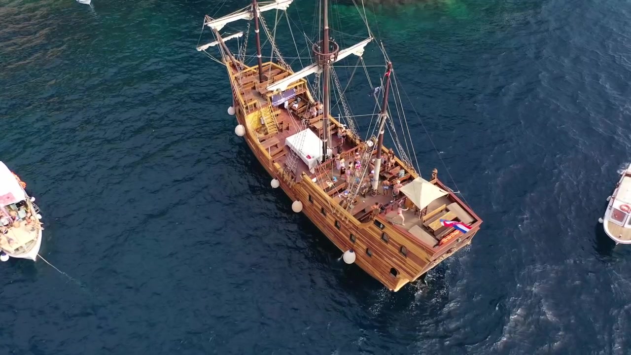 Splendide riprese con drone di una nave in legno in stile storico e barche a vela bianche ancorate in una cala turchese. Presenta spettacolari scogliere calcaree e lussureggianti pinete lungo la soleggiata costa adriatica
